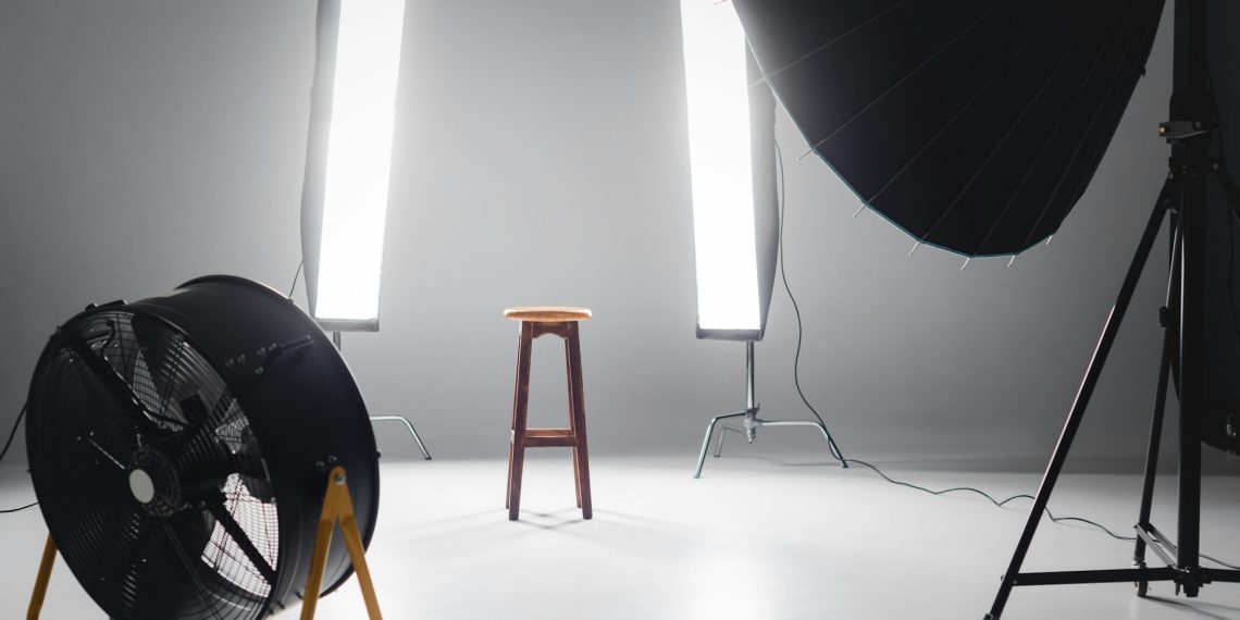 digital camera, fan, reflector, wooden stool and lights on backstage in photo studio